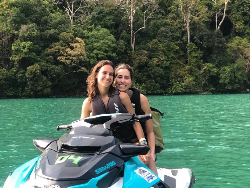 Two guests riding a jet ski with a forested shoreline behind them