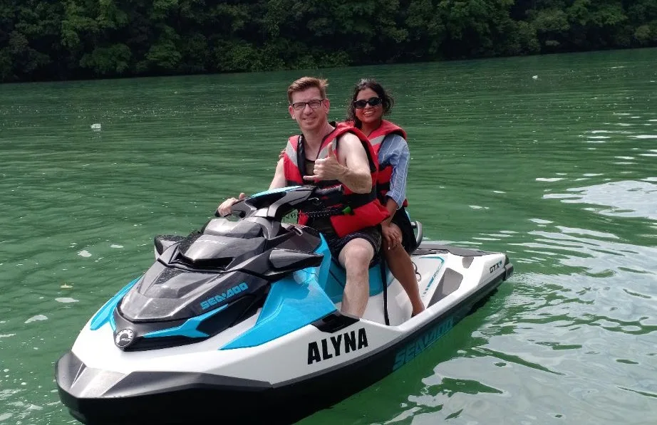 Two guests sharing an Alyna jet ski beside a wooded shoreline